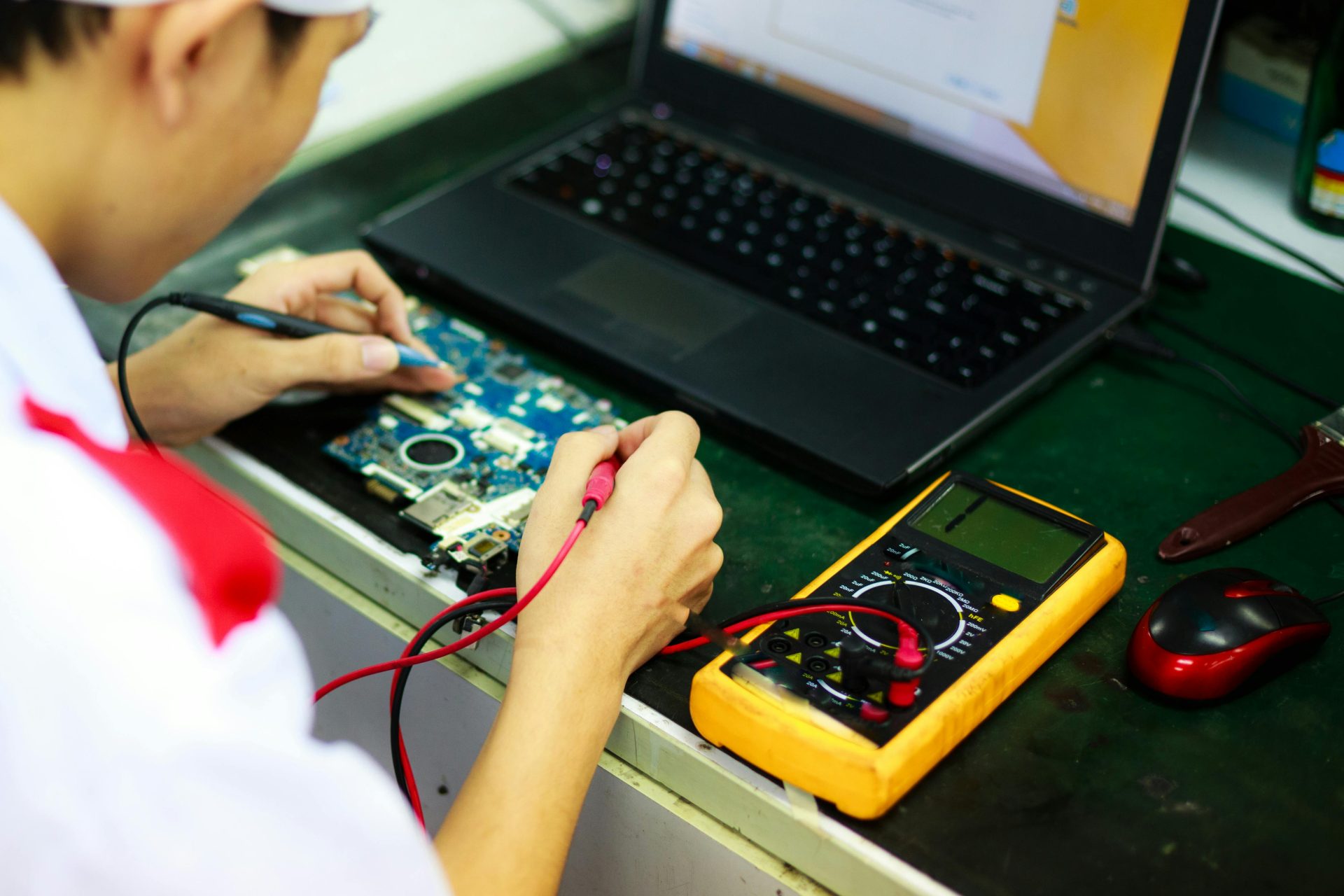 Técnico trabajando en una computadora portátil con multímetro en un espacio de trabajo profesional.